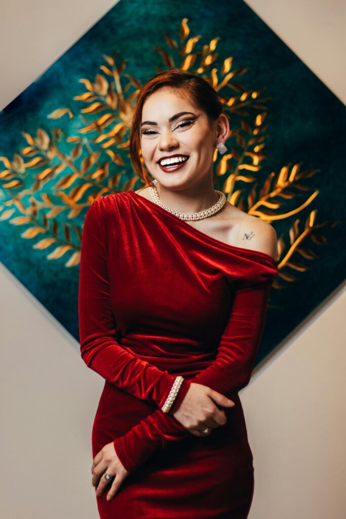 Stylish woman laughing in a red velvet dress against a decorative backdrop.