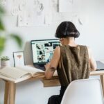 A young creative designer working remotely at her desk with sketches and a laptop.