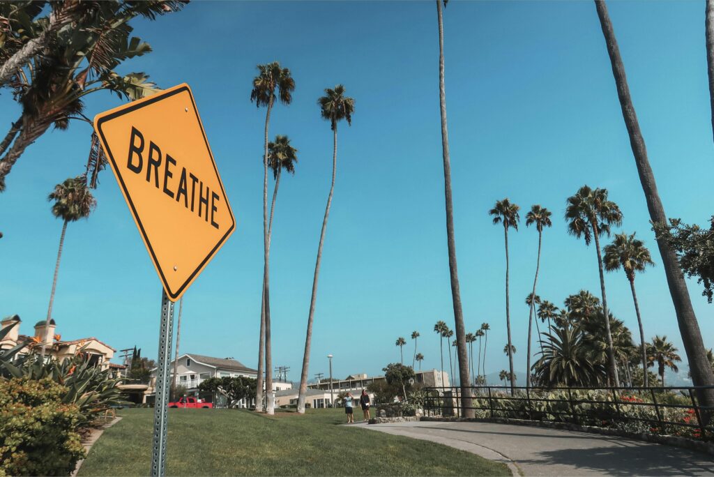 A peaceful street view in Laguna Beach featuring palm trees and a 'Breathe' sign.