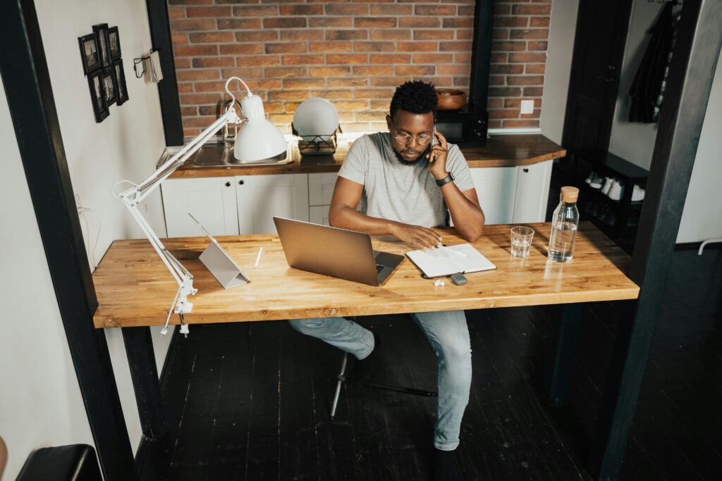 pexels photo 5198240 5198240 A young man at a desk in a home office, using a laptop and phone, embodying remote work lifestyle.