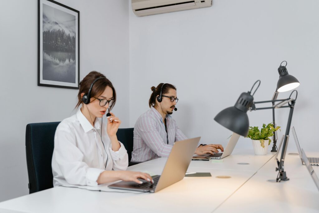 pexels photo 7709088 7709088 1 Two call center agents using laptops and headsets in a modern office setting.