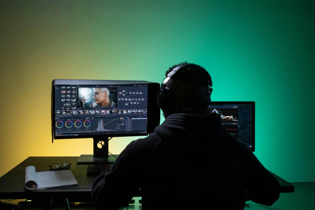 pexels photo 8102677 8102677 A video editor works on dual monitors with headphones, focusing on color correction.
